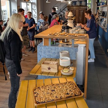 zeigt Blick in die Blaubeerscheune mit Blaubeerkuchen im Vordergrund und sich dort aufhaltenden Personen