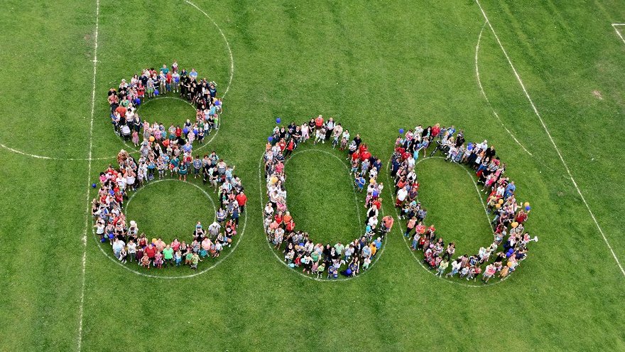 zeigt aus der Vogelperpektive auf einer Wiese eine von Kindern gebildete "800"