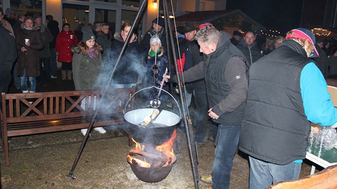 zeigt Personen, die Feuerzangenbowle zubereiten und Festbesucher
