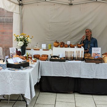 zeigt Marktstand mit gedrechselten Produkten und die Anbieterin