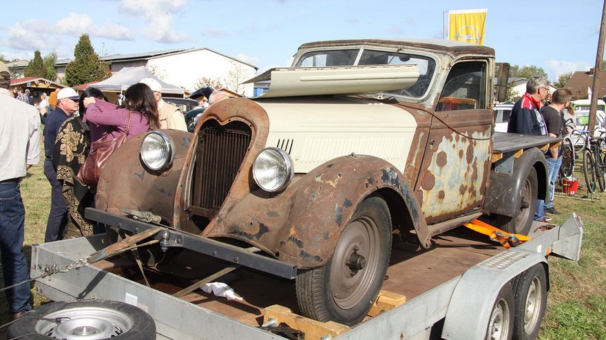 zeigt verrosteten Oldtimer und betrachtende Menschen
