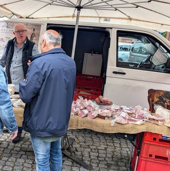 zeigt Marktstand mit Wurstwaren, Anbieter und Besucher
