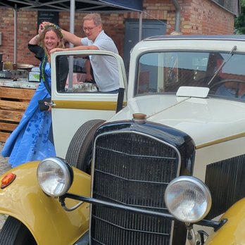 zeigt Oldtimer und 2 Personen, die gerade aussteigen