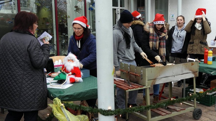 zeigt weihnachtlich kostümierte Kinder und Erwachsene an Markt- und Grillständen vor einem Gebäude