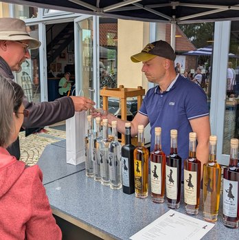 zeigt Tresen eines Marktstandes mit aufgebauten Spirituosenflaschen, den Verkäufer und einen Käufer