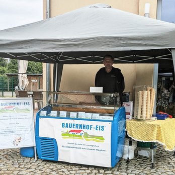 zeigt Marktstand, der Bauernhof-Eis anbietet und einen Mann hinter dem Stand