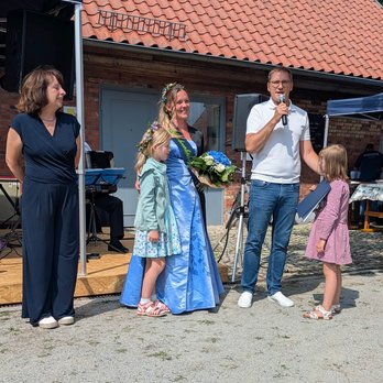 zeigt eine Personengruppe aus 3 Erwachsenen und 2 Kindern, wobei der Mann ins Mikrofon spricht