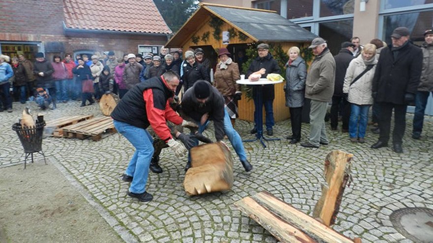 zeigt Männer beim Wettstreit mit Holzstücken und Zuschauergruppen